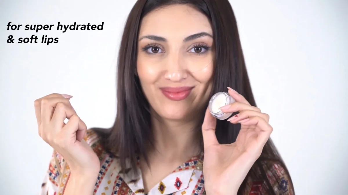 Frame from a beauty product video showing a model smiling at camera and holding an open lip balm jar, with a short native-style caption on the left as used in a Reels hook test
