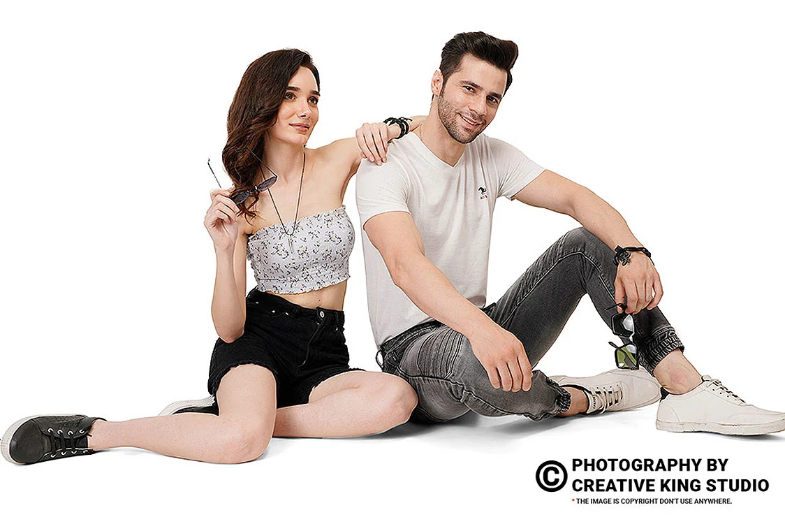 Two models seated on a white studio floor in casual tops, denim and sneakers, a styled on-model apparel frame used as the scale image in a listing sequence