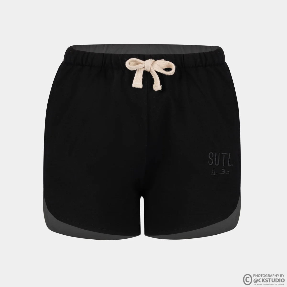 Black drawstring lounge shorts with grey side panels shot on an invisible mannequin against a light background, showing waistband and hem construction