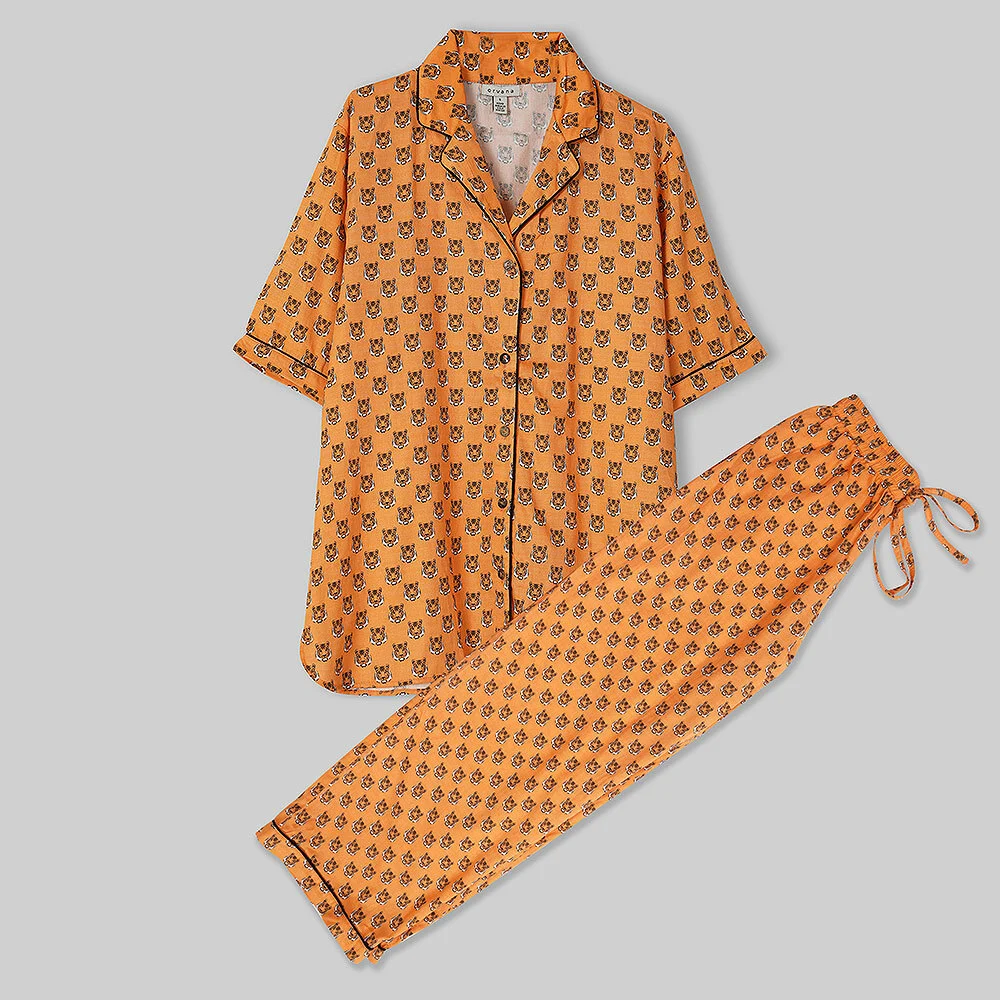 Orange printed night suit set laid flat on a light grey surface with shirt collar and drawstring trousers visible, a clean apparel flat lay catalogue frame