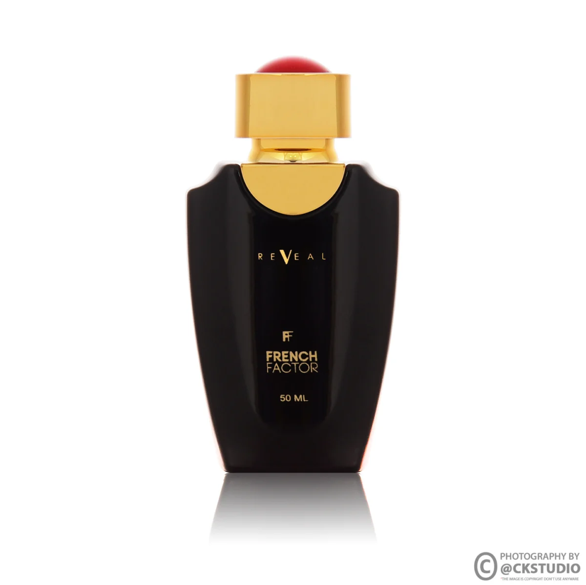 Black fragrance bottle with a gold collar and red cap on white, its glossy shoulders lit by soft strip highlights with a mirror reflection below