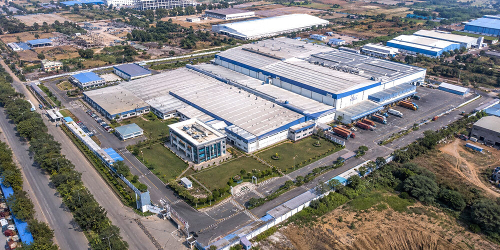 Aerial drone photography of a large Indian industrial corporate facility shot from above showing factory roof, warehouses, parking area and surrounding infrastructure for brand and investor presentations