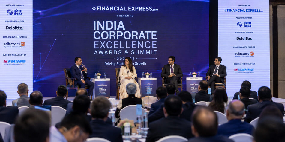 Corporate event photography of a panel discussion with branded stage backdrop and engaged audience at an Indian business summit covered by Ckstudio