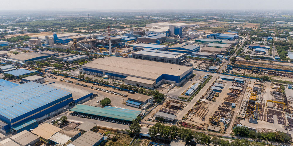 Aerial drone filming of a large industrial manufacturing plant showing multiple sheds, logistics yard and warehouse rooftops from above, daytime establishing shot for corporate film