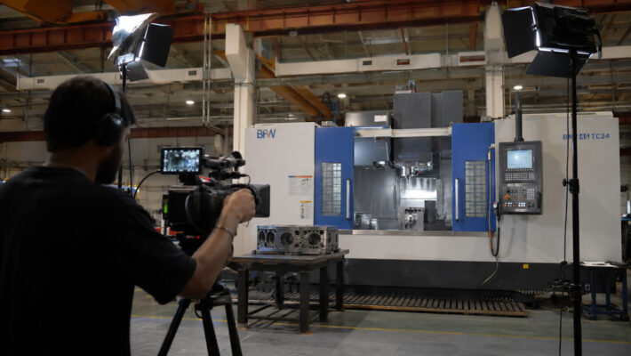 Professional industrial videographer filming a CNC machine in operation inside an Indian manufacturing plant with professional video lighting setup.