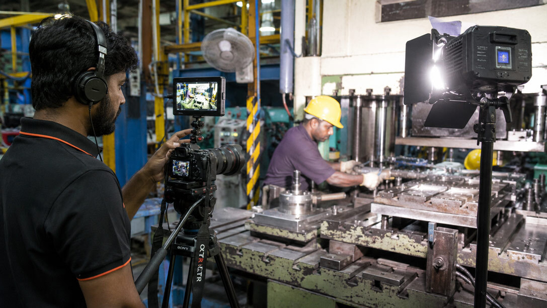 Professional video production crew filming a manufacturing process on a factory floor with cinema camera and lighting for industrial photography & videography
