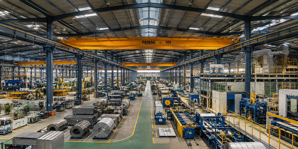 Large Indian manufacturing facility shot using panoramic industrial photography in India with wide-angle stitched view of production lines, overhead cranes and warehouse interiors under controlled lighting