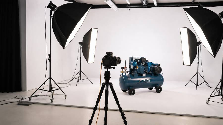 Cinematic behind the scenes of a professional product photography shoot at a Delhi studio, photographer tethered to a laptop capturing a small product on a white shooting table with two glowing softboxes