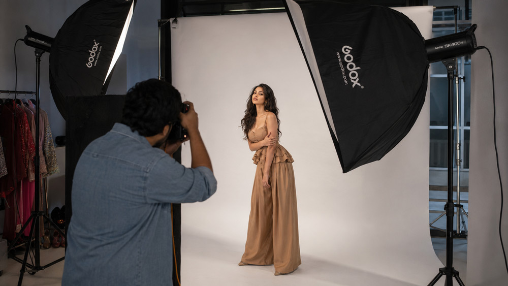 Editorial fashion photography behind the scenes at a Delhi studio with softbox lighting, cyclorama backdrop, model in styled outfit, photographer directing pose, professional atmosphere, high fashion aesthetic, documentary photography style
