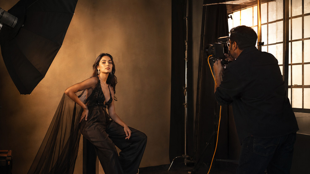 Editorial fashion photography shoot in Delhi NCR studio with dramatic lighting, model in high-fashion styling, professional photographer with medium format camera, moody backdrop, warm golden hour light