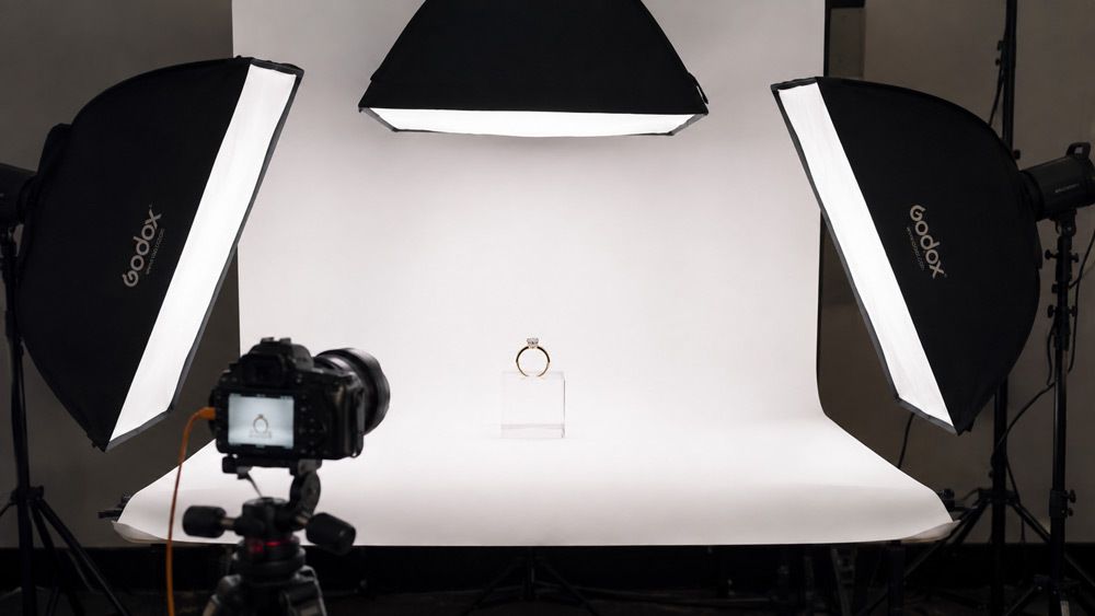 Studio setup for white background jewellery photography showing diamond ring on acrylic block with three softbox lighting configuration