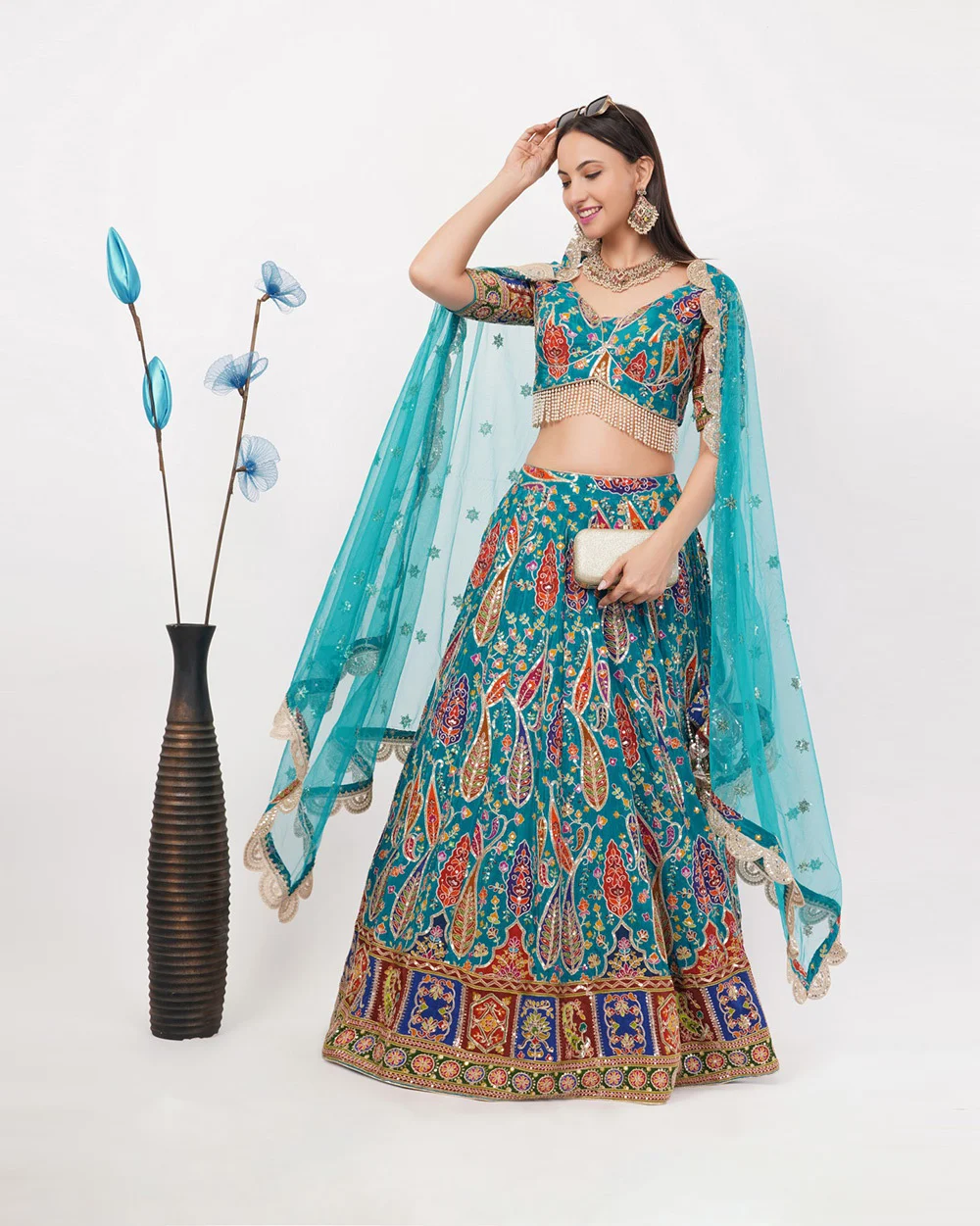 Indian female model in a turquoise embroidered lehenga choli posing on a light grey studio background in a portrait 4 by 5 frame, the kind of on-model first image that leads an apparel gallery