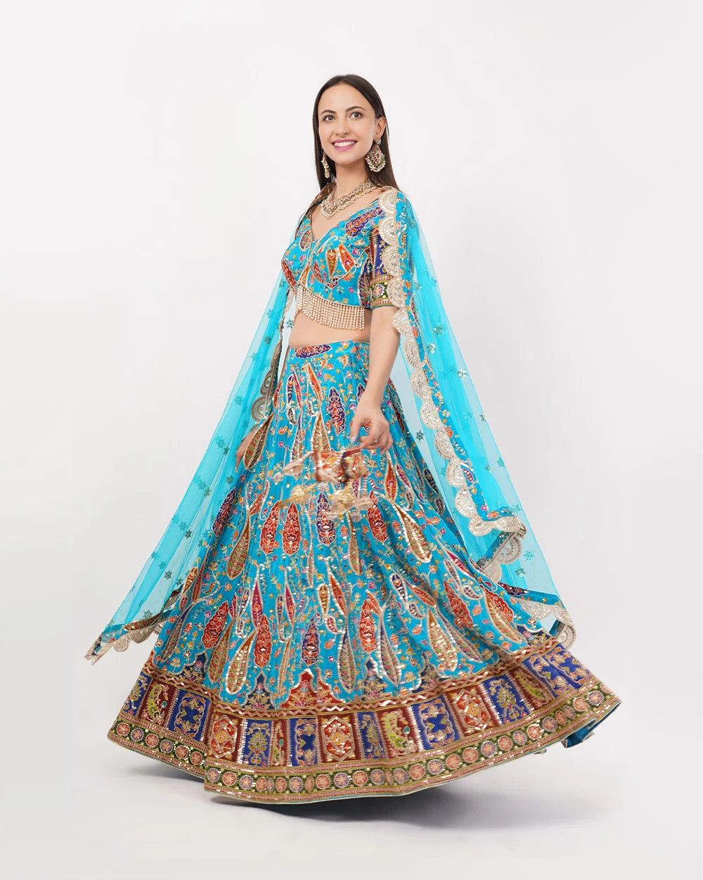 Full-length portrait catalogue photo of a model in a turquoise embroidered lehenga choli on a clean light backdrop, framed tall for a fashion marketplace gallery