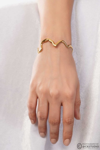 Ckstudio shot of gold wavy bracelet on hand against soft white fabric background, Commercial Product Photography