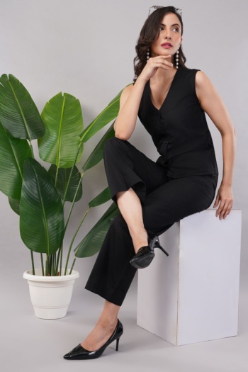B) model wearing black sleeveless top and pants, seated on white block with green plant, Commercial Product Photography shot — Ckstudio