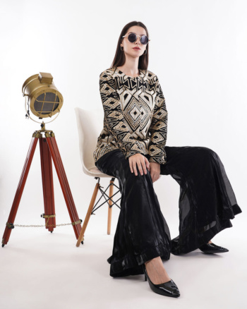 B) model wearing patterned top and black wide-leg pants, seated on white chair with vintage lamp, Commercial Product Photography shot — Ckstudio