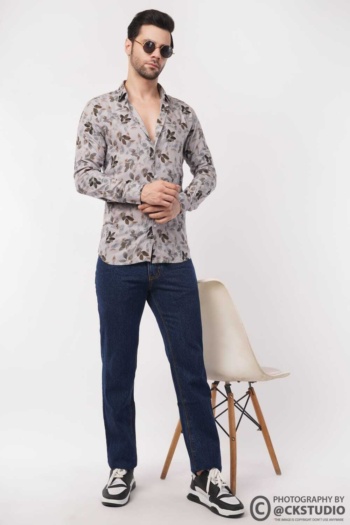 B) man wearing floral shirt and jeans, standing by white chair on white background, Fashion Photography shot — Ckstudio