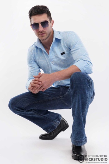 B) man wearing blue patterned shirt and jeans, crouching on white background, Fashion Photography shot — Ckstudio
